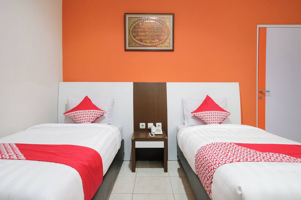 Habitación de hotel con dos camas, una mesita de noche con teléfono y un objeto enmarcado en la pared.