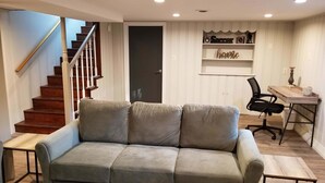 Un salon avec un canapé gris, un escalier en bois, une porte et un bureau avec une chaise.