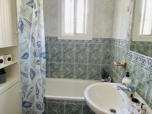 Bathroom features a sea shell and starfish patterned shower curtain, a bathtub, and a white sink with a chrome faucet.