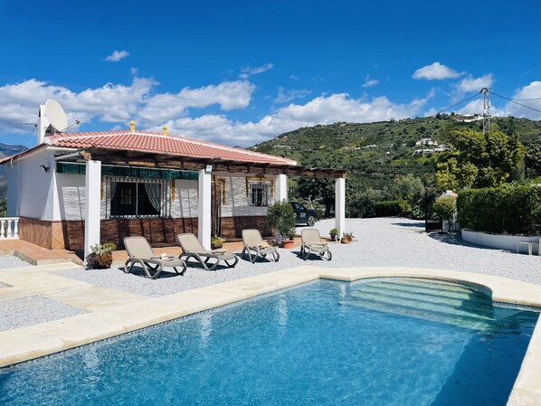 Relax by the serene pool surrounded by lush green hills and lounge chairs.