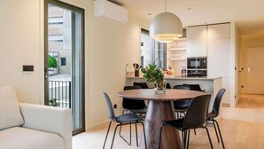 A modern apartment with a dining area featuring a round table and black chairs, a white sofa, and a large window overlooking a cityscape.