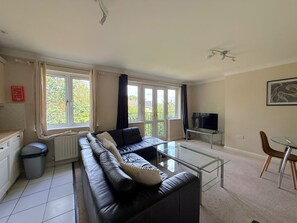 A living room with a black leather sofa, a glass coffee table, and a TV on a stand.