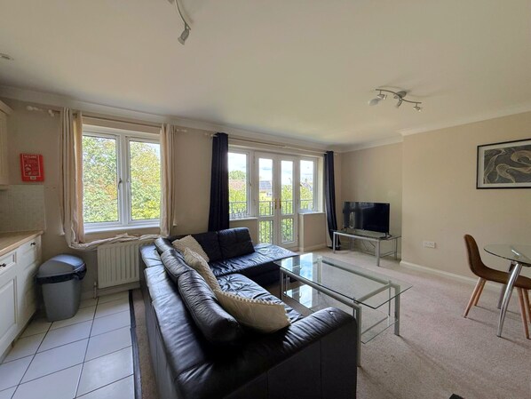 A living room with a black leather sofa, a glass coffee table, and a TV on a stand.