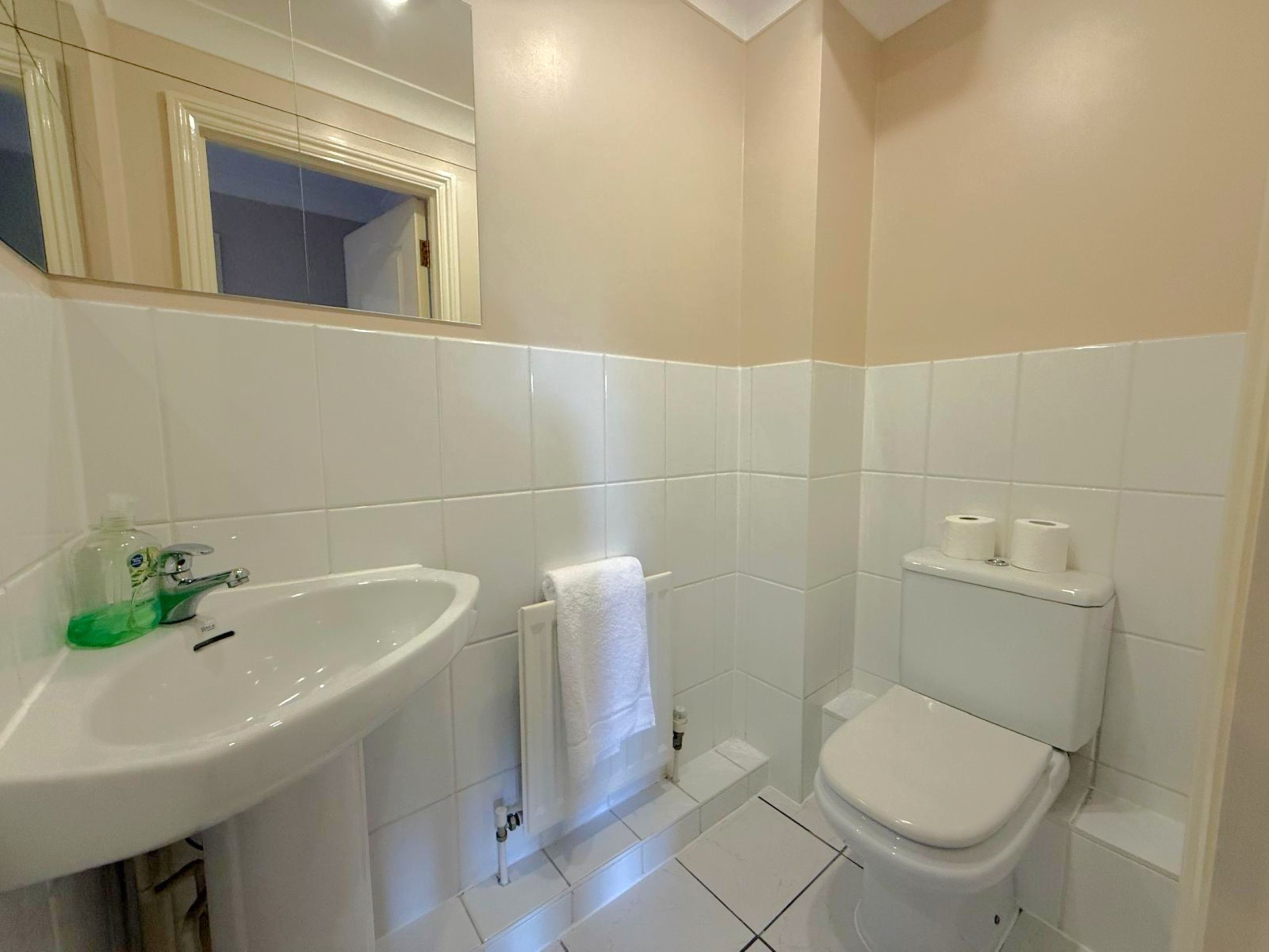 Et badeværelse med en hvid vask, toilet og et spejl over vasken.
