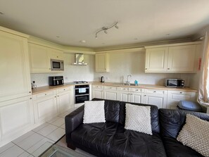 A compact kitchen with white cabinets, a black leather sofa with decorative pillows, and a microwave on the countertop. - Spacious Two Bedroom Apartment in Bracknell (Bracknell)