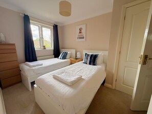 A hotel room with two beds, a dresser, a window with curtains, a wall clock, and a door.