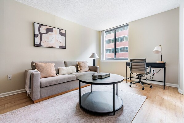 Relax in this stylish living room with a comfortable sofa, coffee table, and desk, offering a peaceful view of the surrounding cityscape.