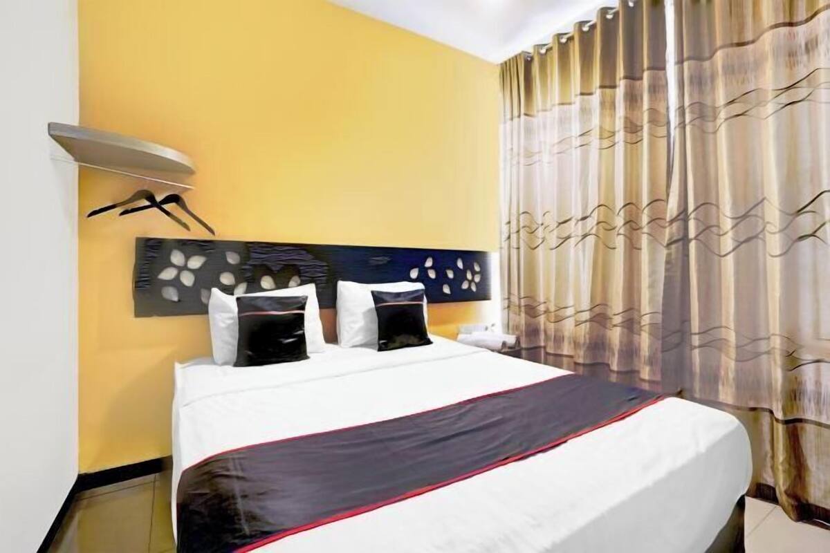 Hotelkamer met een bed, een hoofdeinde met een decoratief paneel, een wandlamp en een gordijn met een golvend patroon.