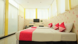 Ein Hotelzimmer mit zwei Betten, einem Schreibtisch, einem Fernseher und großen Fenstern mit Vorhängen.