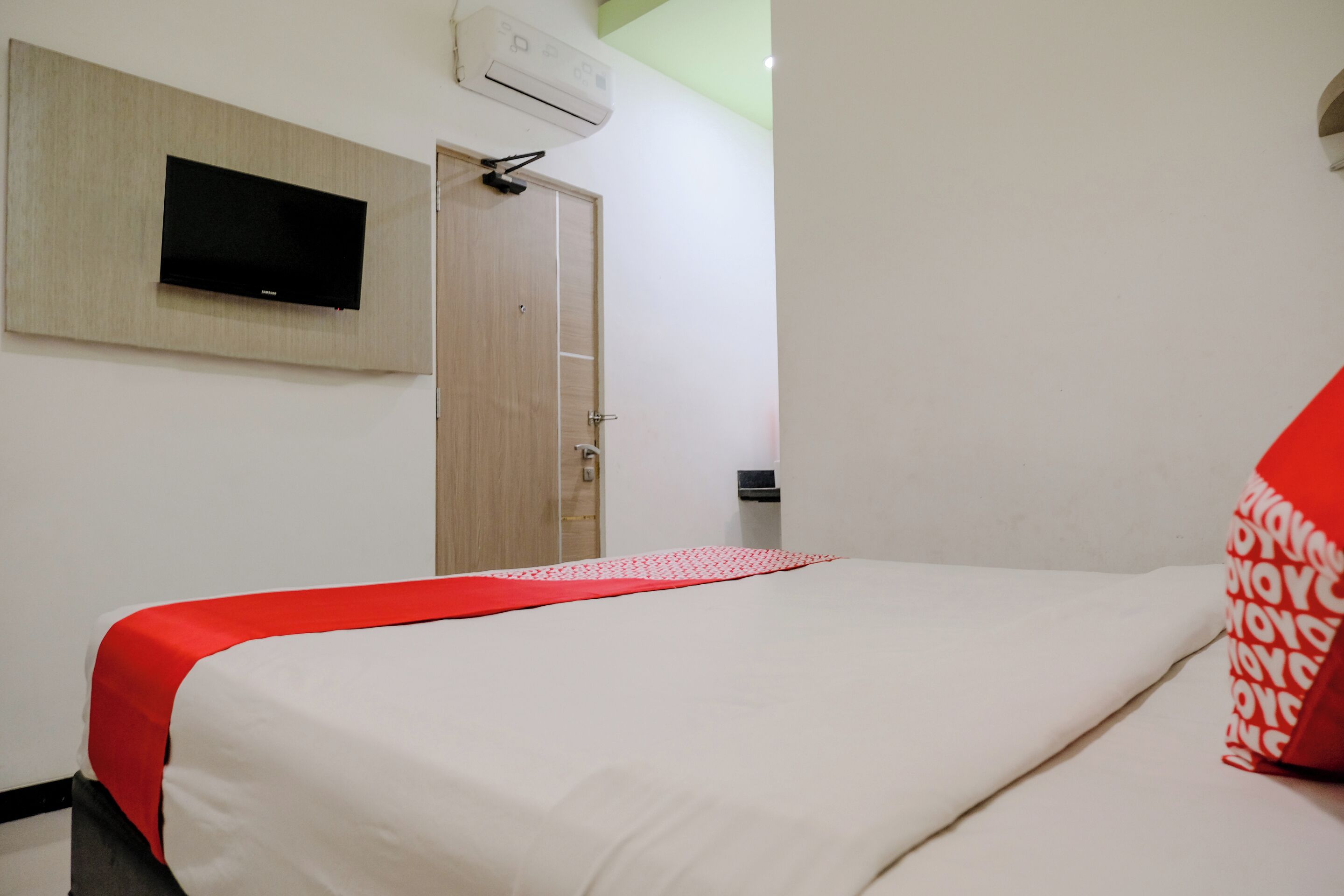Ein Hotelzimmer mit Bett, Wandfernseher und Klimaanlage über der Tür.