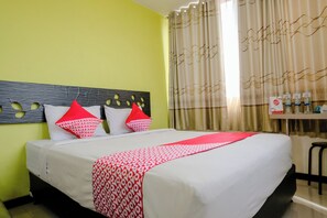 Habitación de hotel con cama, cabecera con diseños de hojas y una colcha estampada en rojo y blanco, además de una mesa con artículos de aseo.