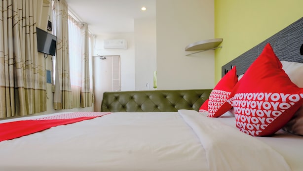 Ein Hotelzimmer mit einem dunkelgrünen, gepolsterten Kopfteil, weißer Bettwäsche und roten Kissen.