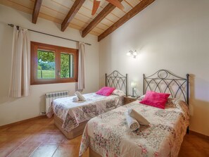 Une chambre avec deux lits, une fenêtre avec des rideaux, un radiateur et un ventilateur de plafond.