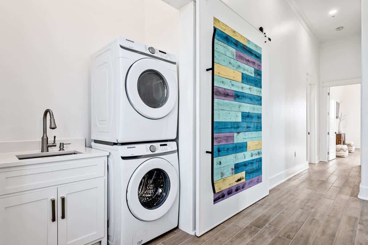 A laundry area with stacked washers and dryers, a sink, and a colorful wooden panel wall.