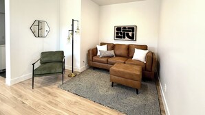 Ein modernes Wohnzimmer mit einem grünen Sessel, einem braunen Sofa, einem schwarz-weißen Teppich und einer Stehlampe.