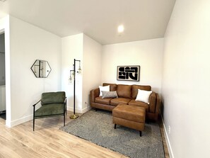 A modern living room with a green armchair, a brown sofa, a black and white rug, and a floor lamp.