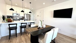 Una cocina moderna con una isla central, taburetes de bar, iluminación colgante y un televisor de pantalla plana montado en la pared.