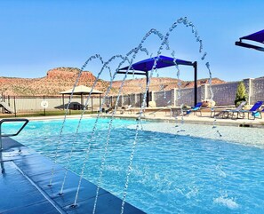 Una piscina con chorros de agua, sillones de descanso y vistas a colinas de roca roja.