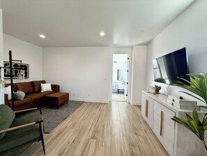 A modern living room with a brown sofa, a green armchair, a wooden floor, a white wall, and a TV mounted on the wall.