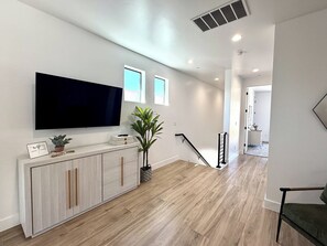 Un salon moderne avec un téléviseur à écran plat, un meuble en bois, une plante en pot et un escalier menant à une autre pièce.