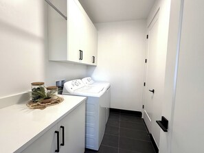 Ein Waschraum mit Waschmaschine, Wäscheständer und einer Arbeitsplatte mit Gläsern und einer Pflanze.