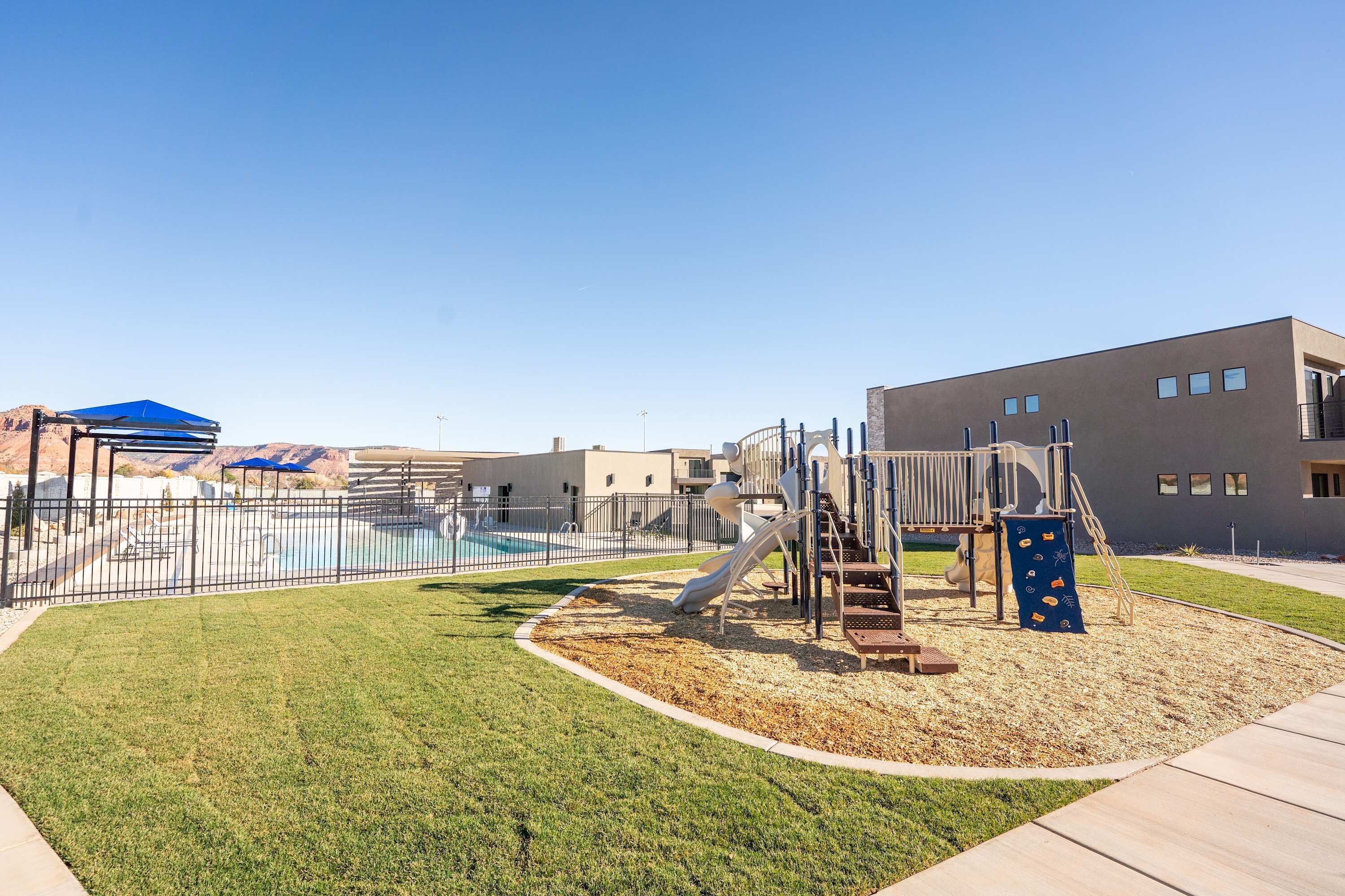A playground with a slide, climbing structures, and a fenced pool area.
