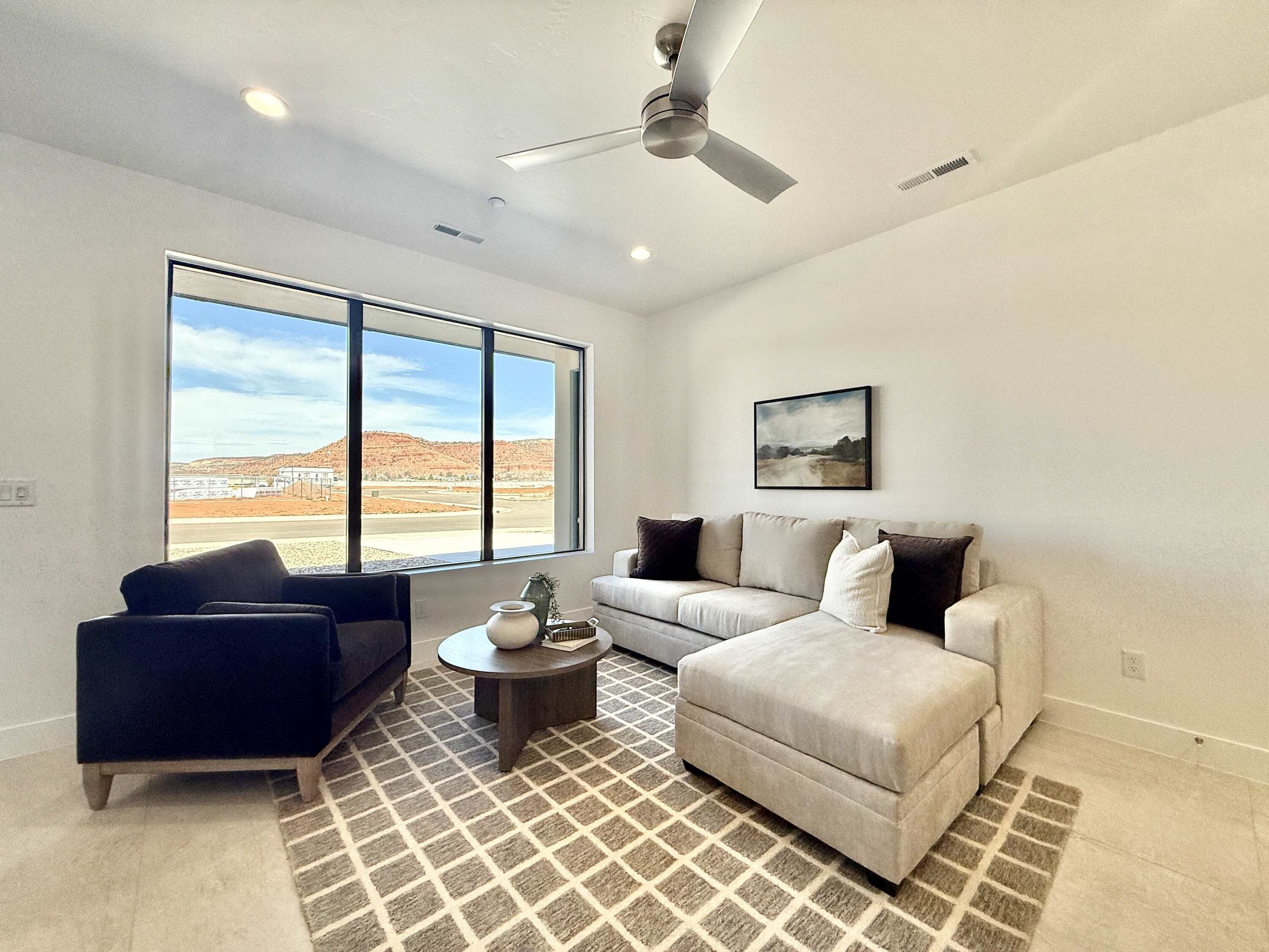 A modern living room with a large window, a ceiling fan, and a view of a desert landscape.