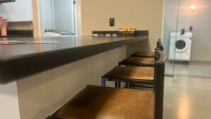 A kitchen area with a counter and three stools. There is a washing machine in the background.