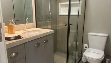 Een moderne badkamer met een douchecabine van glas, een toilet en een wastafel met aanrechtblad.