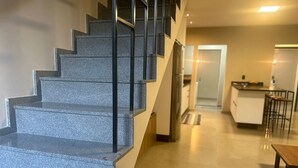 A staircase with a modern design, leading to a kitchen area with a bar and a dining table.
