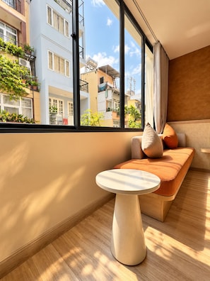 A modern living room with a large window, a round table, and a sofa with cushions. - KOVA Hotel - Bui Vien Central (Ho Chi Minh City)