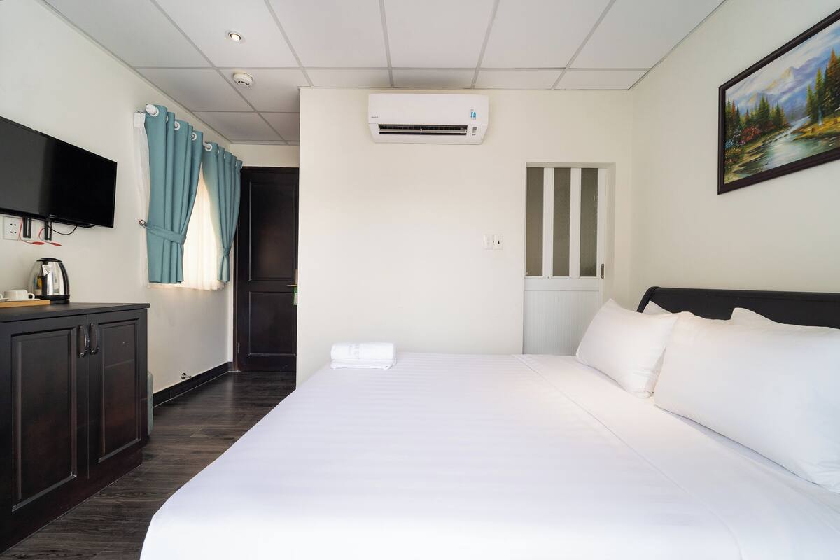 Une chambre d’hôtel avec un lit, une télévision, un climatiseur, un tableau et une fenêtre avec des rideaux.