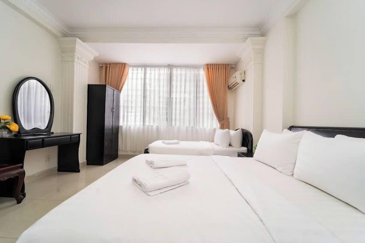 Une chambre d’hôtel avec deux lits, un bureau, une armoire et un grand miroir.