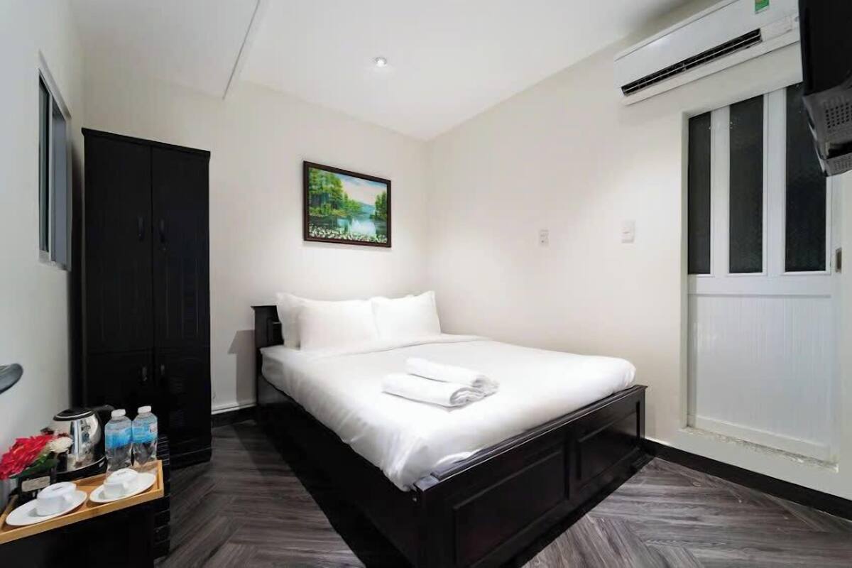 Une chambre d’hôtel avec un lit, une table de chevet avec des articles de toilette, un tableau au mur et une fenêtre avec des stores.