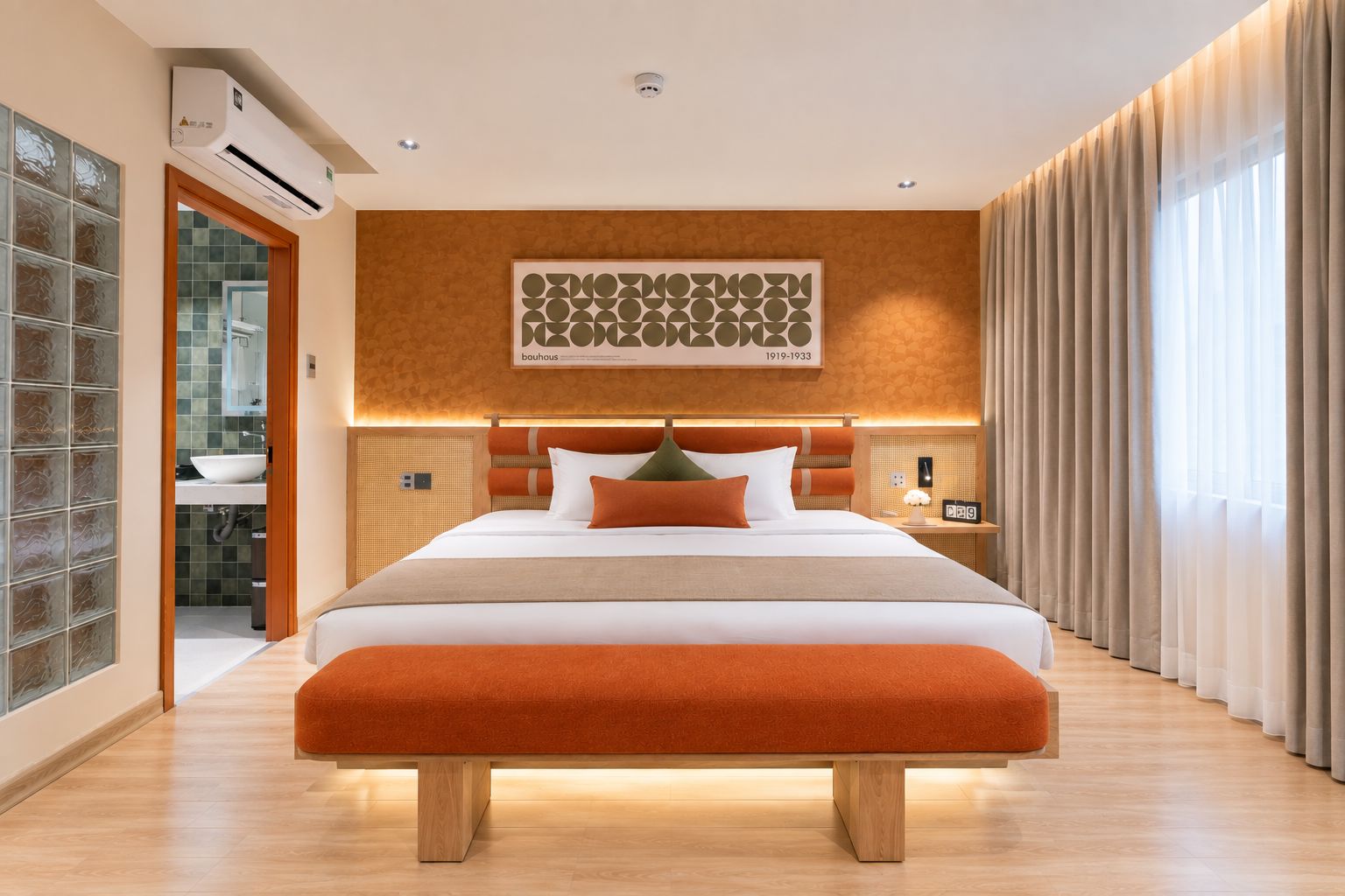 Ett modernt hotellrum med en stor säng, ett badrum med en glasvägg och en väggmonterad luftkonditioneringsanläggning.