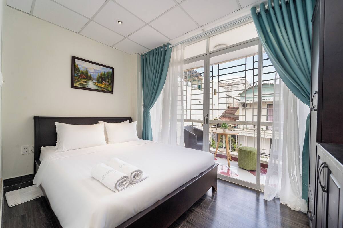 Une chambre d’hôtel avec un grand lit, un tableau au mur et un balcon donnant sur des immeubles.
