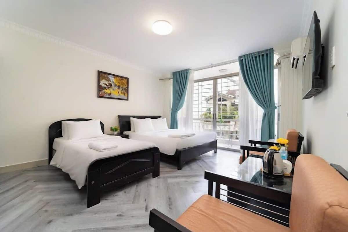 Une chambre d’hôtel avec deux lits, une table à manger, un téléviseur fixé au mur et un balcon avec des rideaux.