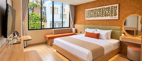 Ein Hotelzimmer mit Bett, Schreibtisch, Stuhl, einem Fenster mit Blick auf Gebäude und einem an der Wand befestigten Kunstwerk.