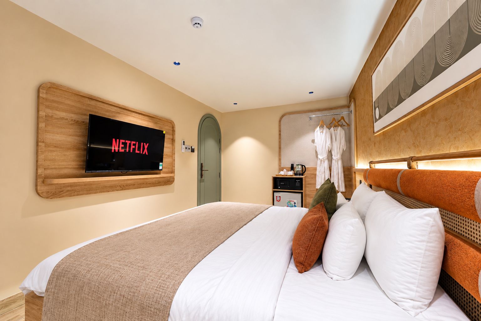 A hotel room with a bed, a television mounted on the wall, a door, and a small table with a kettle.