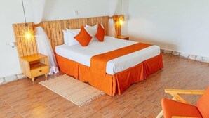 A bedroom with a wooden headboard, a bed with white and orange bedding, a nightstand, a chair, and a rug. - Acacia Wilderness Mweya (Mweya)