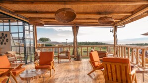 A wooden deck with orange chairs and tables, large windows, and a view of the landscape. - Acacia Wilderness Mweya (Mweya)
