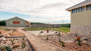 A modern house with a stone exterior, a paved pathway, and a landscaped garden with rocks and cacti. - Acacia Wilderness Mweya (Mweya)