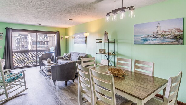 A dining area with a wooden table and chairs, a sofa, and a view of the balcony.