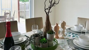 A dining table set with white plates, bowls, and glasses, a bottle of red wine, and decorative items including a vase and a branch sculpture. - Cityside retreat by QEII&QSAC (Coopers Plains)