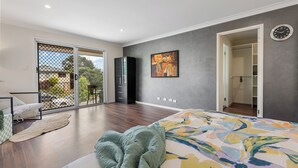 A modern bedroom with a large bed, a sliding glass door leading to a balcony, a wardrobe, and a painting on the wall. - Cityside retreat by QEII&QSAC (Coopers Plains)