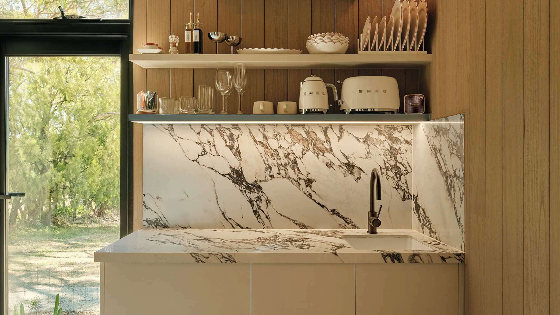 A kitchen with a marble backsplash, a built-in sink, and a window overlooking greenery.