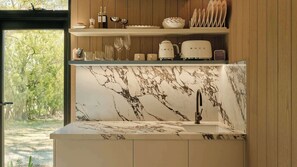 A kitchen with a marble backsplash, a built-in sink, and a window overlooking greenery.