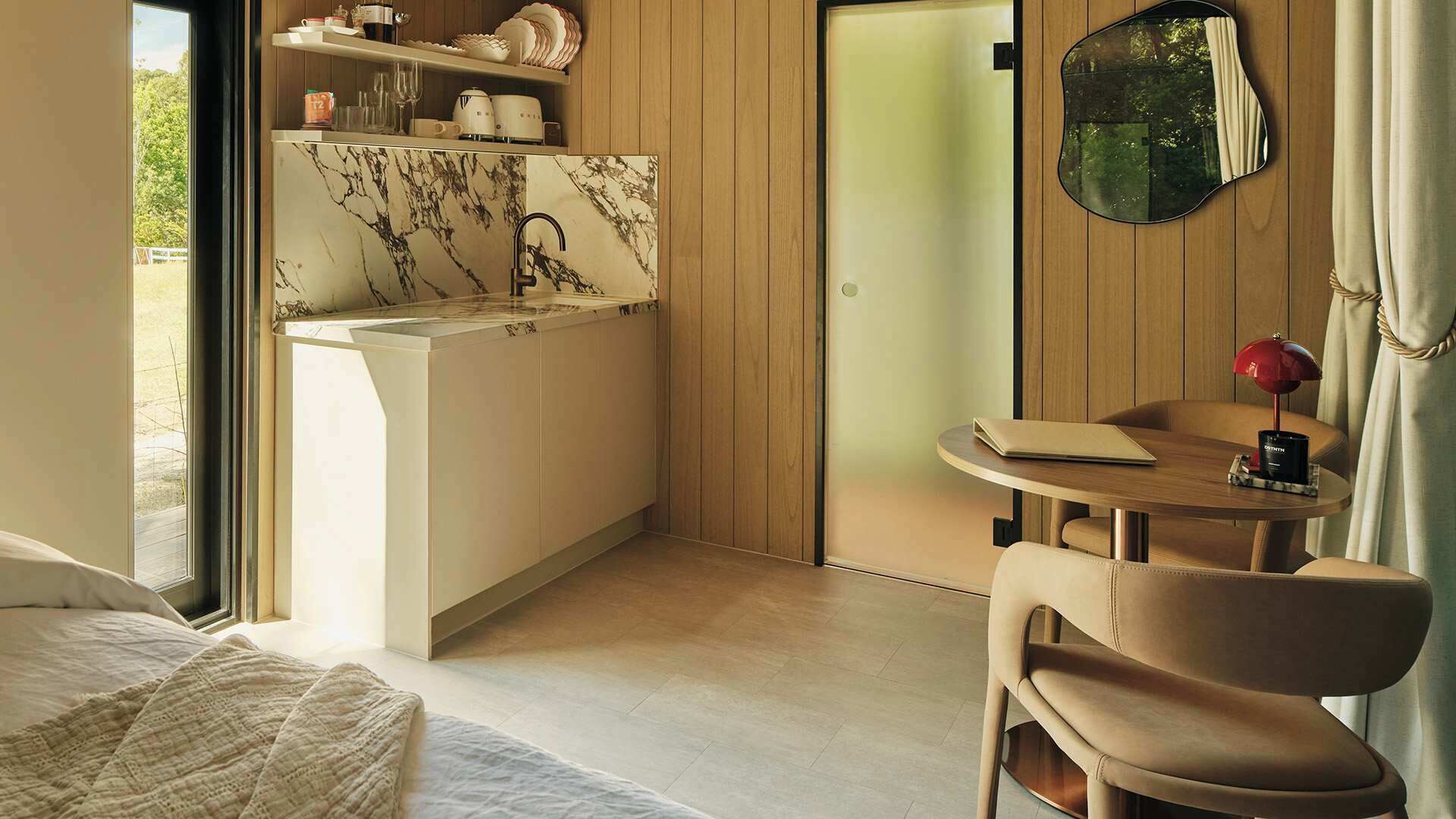 A compact hotel room with a kitchenette, a bed, a small table with a chair, and a mirror.