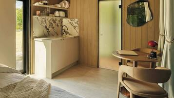 A compact hotel room with a kitchenette, a bed, a small table with a chair, and a mirror.