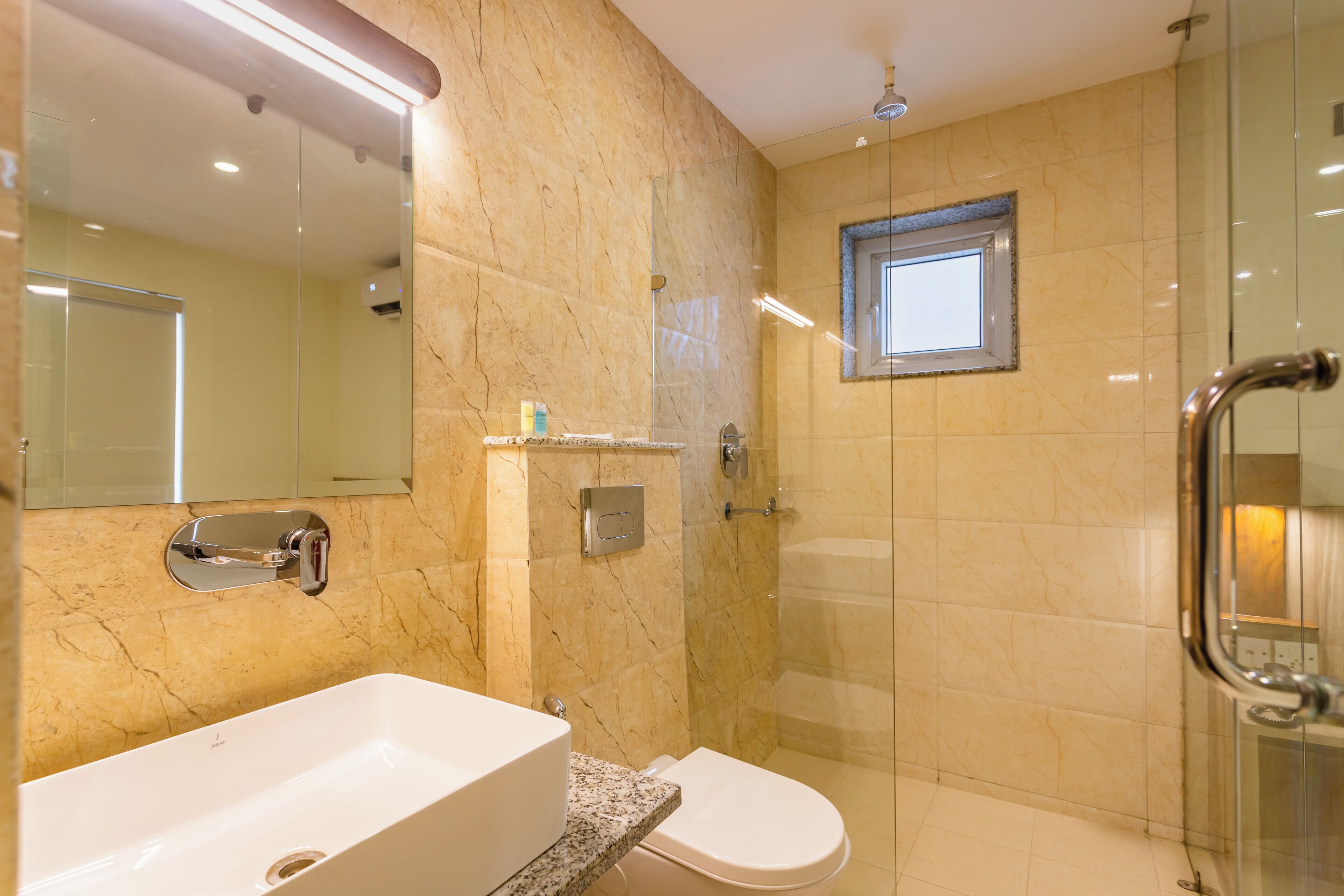 Un baño moderno con un lavamanos grande de color blanco, un inodoro y una zona de ducha con mampara de cristal.